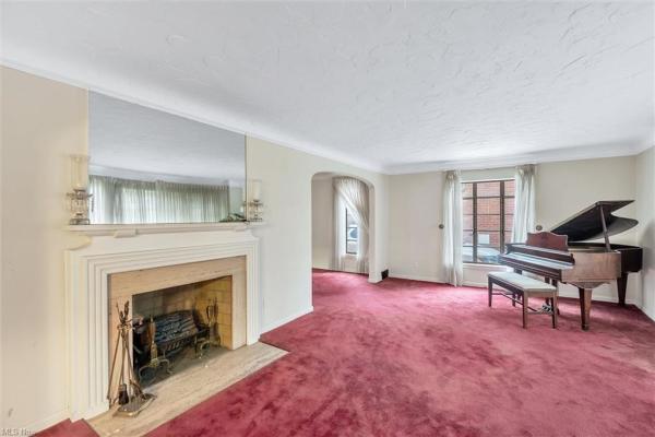 Living room with fireplace, piano, wine-colored carpeting, and floor-length windows in Cleveland, Ohio house for sale, listed by Will Davis, Ohio probate specialist and realtor