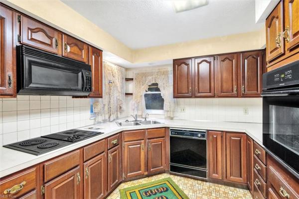 Kitchen with earth-toned tile floor, white tile backsplash, black kitchen appliances, &amp; dark wood cabinetry in Cleveland, Ohio house for sale, listed by Will Davis, Ohio probate specialist and realtor