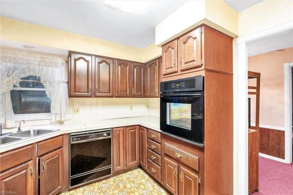 Kitchen with earth-toned tile floor, white tile backsplash, black kitchen appliances, &amp; dark wood cabinetry, shot facing dining room in Cleveland, Ohio house for sale, listed by Will Davis, Ohio probate specialist and realtor