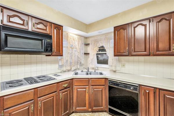 Closeup of kitchen with earth-toned tile floor, white tile backsplash, black kitchen appliances, &amp; dark wood cabinetry in Cleveland, Ohio house for sale, listed by Will Davis, Ohio probate specialist and realtor