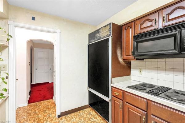 Kitchen with earth-toned tile floor, white tile backsplash, black kitchen appliances, &amp; dark wood cabinetry, shot facing hallway in Cleveland, Ohio house for sale, listed by Will Davis, Ohio probate specialist and realtor