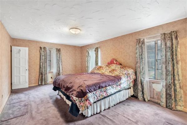 Bedroom with dusky colored walls, floral curtains, floral bedding on large bed with purple comforter, light purple carpeting  in Cleveland, Ohio house for sale, listed by Will Davis, Ohio probate specialist and realtor