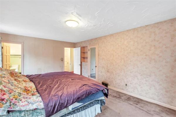 Bedroom with dusky colored walls, floral curtains, floral bedding on large bed with purple comforter, light purple carpeting, shot leading to bathroom and hallway in Cleveland, Ohio house for sale, listed by Will Davis, Ohio probate specialist and realtor