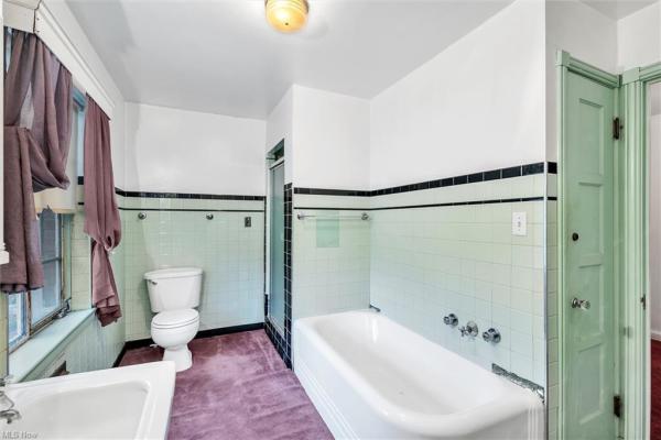 Bathroom with porcelain tub, light green and black colored wall tiles, purple carpeting in Cleveland, Ohio house for sale, listed by Will Davis, Ohio probate specialist and realtor
