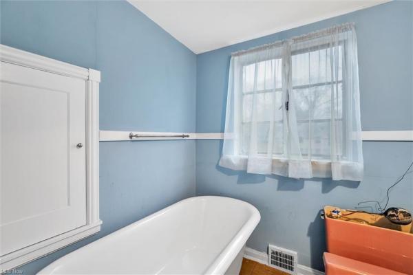 Bathroom with porcelain tub, light blue walls, white cabinet, and window in Cleveland, Ohio house for sale, listed by Will Davis, Ohio probate specialist and realtor