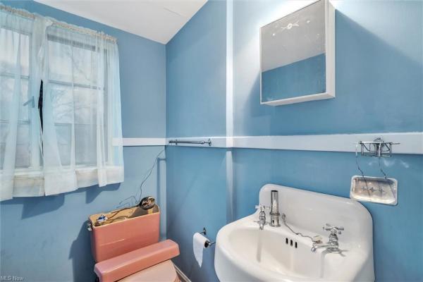 Bathroom with coral toilet, light blue walls, and window in Cleveland, Ohio house for sale, listed by Will Davis, Ohio probate specialist and realtor